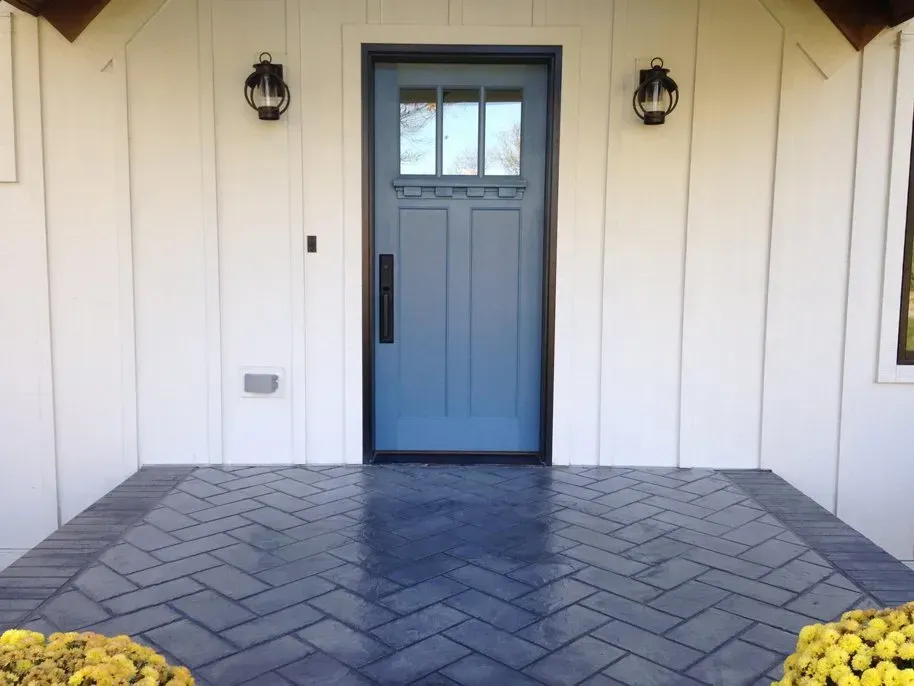 Front porch with a blue front door, white siding, wall lanterns, and a gray paver walkway