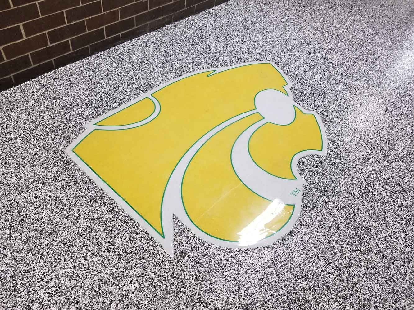 Yellow cougar logo on speckled floor near a brick wall.