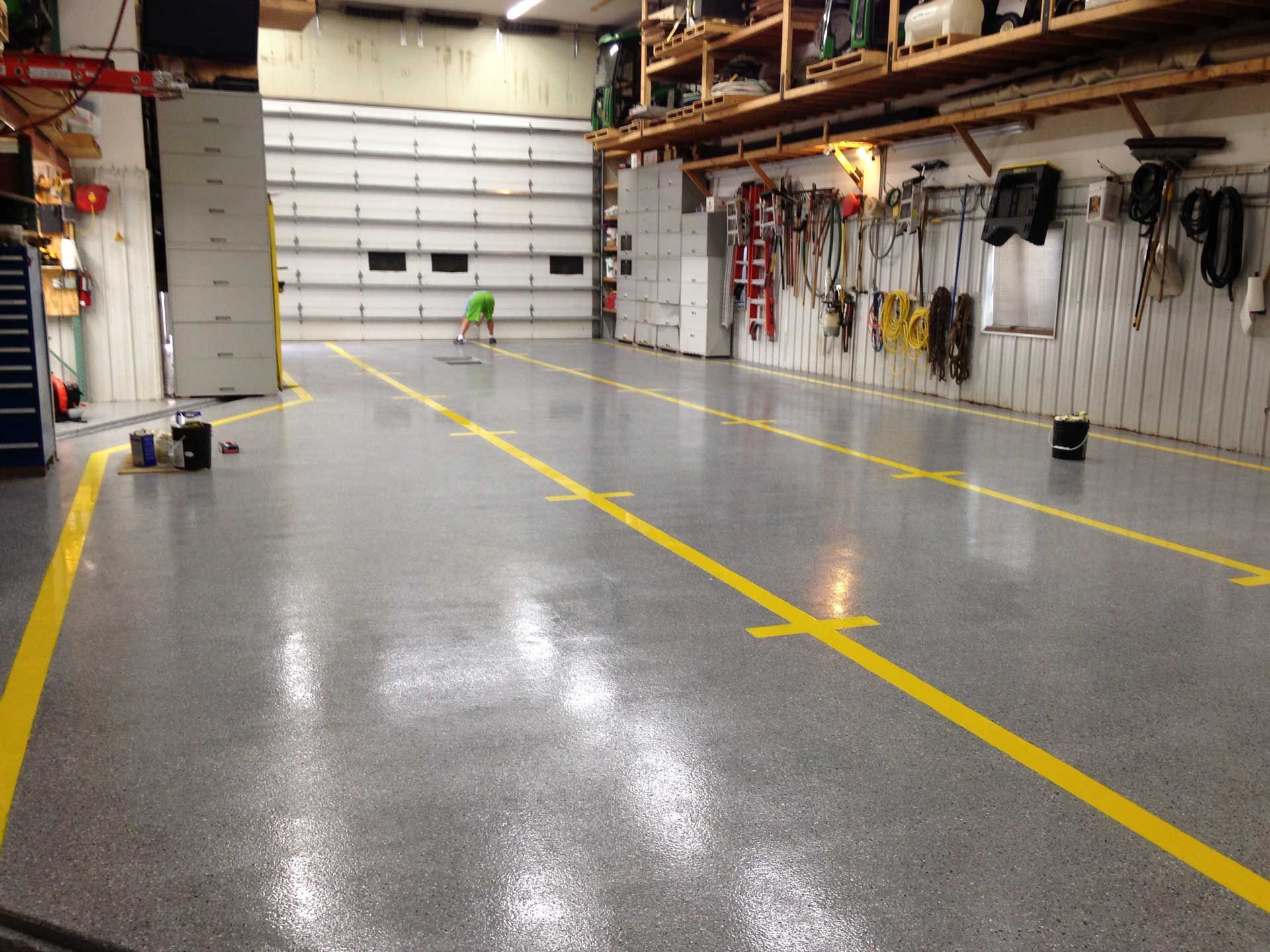 Empty workshop with a glossy gray floor, yellow lane markings, and tools hanging on the walls.