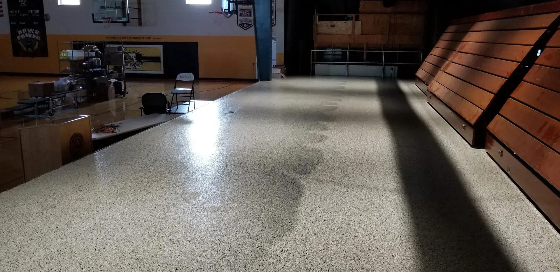 Empty gymnasium with glossy floor and wooden bleachers along the right wall