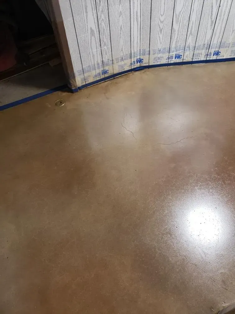 Empty brown floor beside a wall with protective sheeting and blue tape