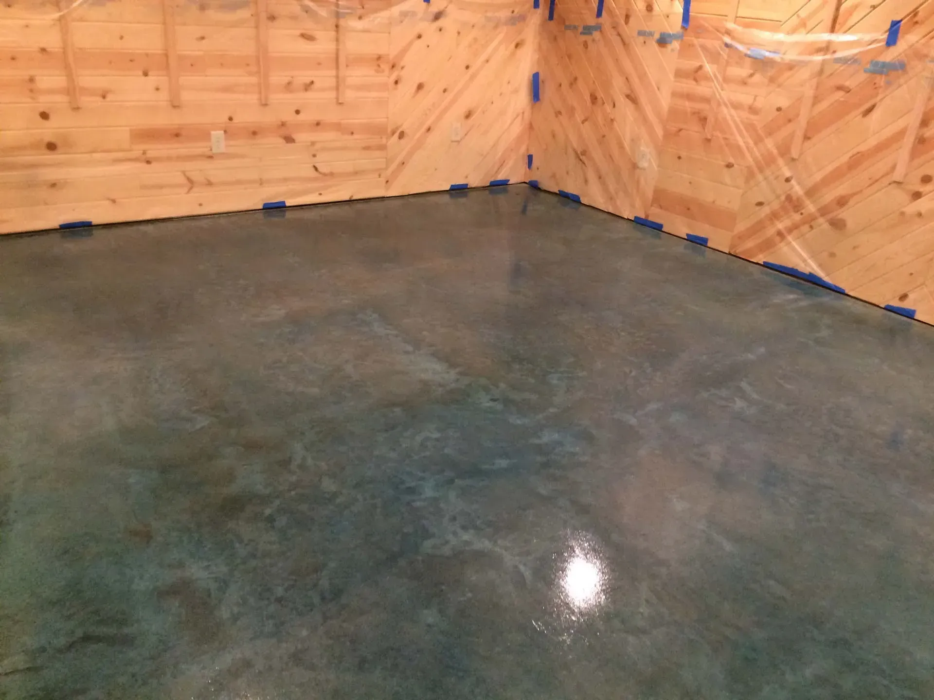 Polished concrete floor in a plywood-walled room with blue tape along the baseboards.