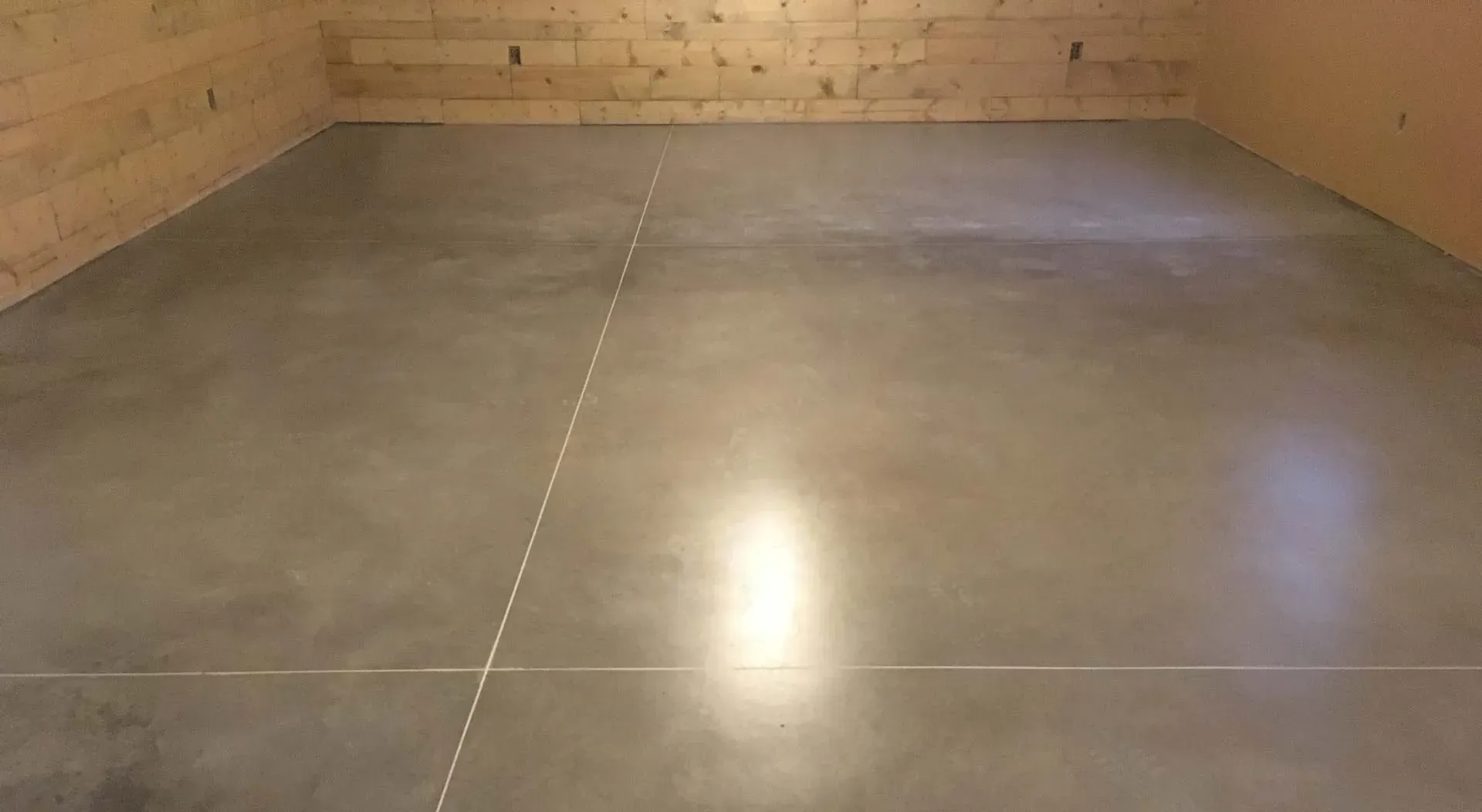 Empty concrete-floored room with wood-paneled walls and a bright light reflection on the floor