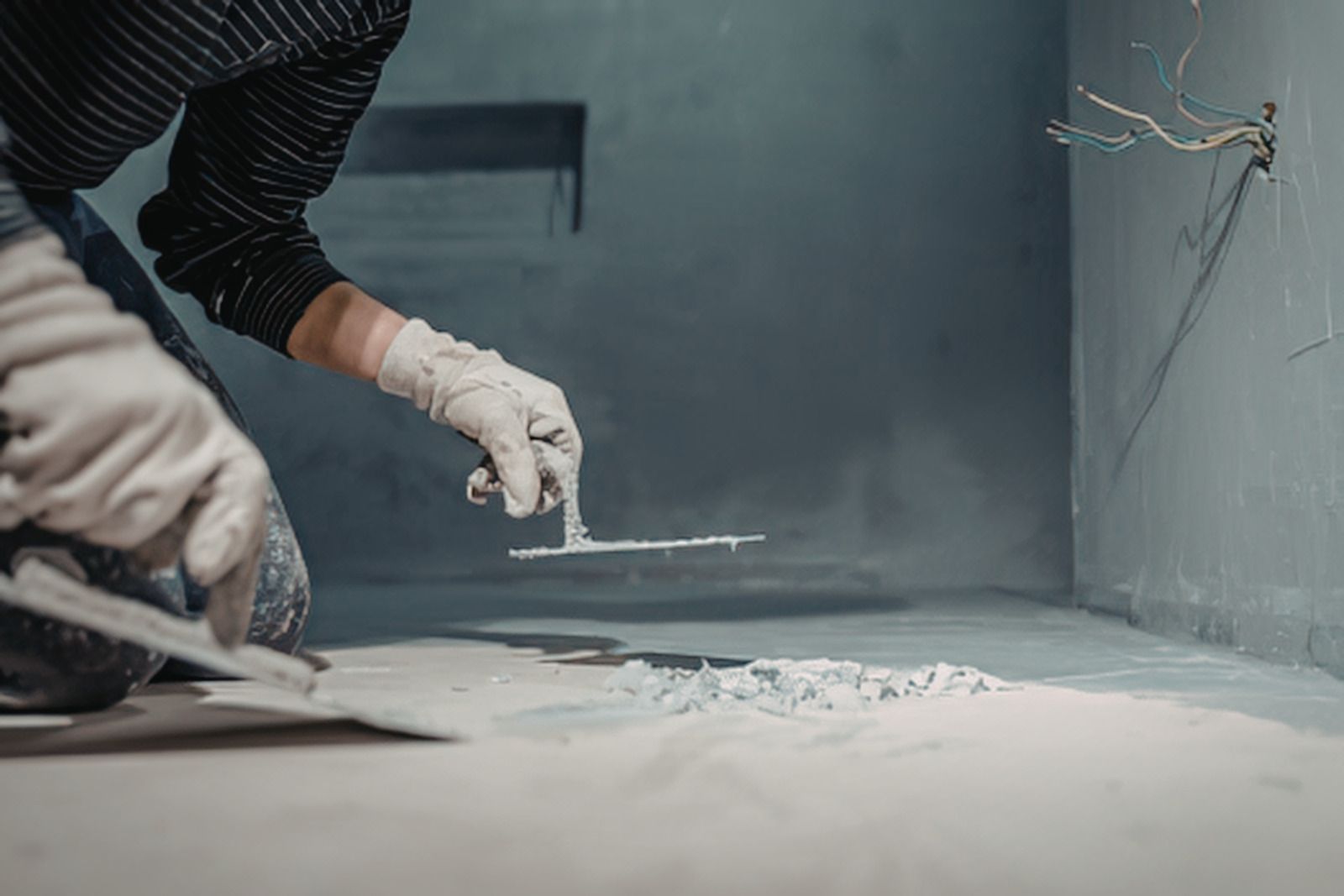 Gloved worker smoothing gray plaster on a wall in an unfinished room