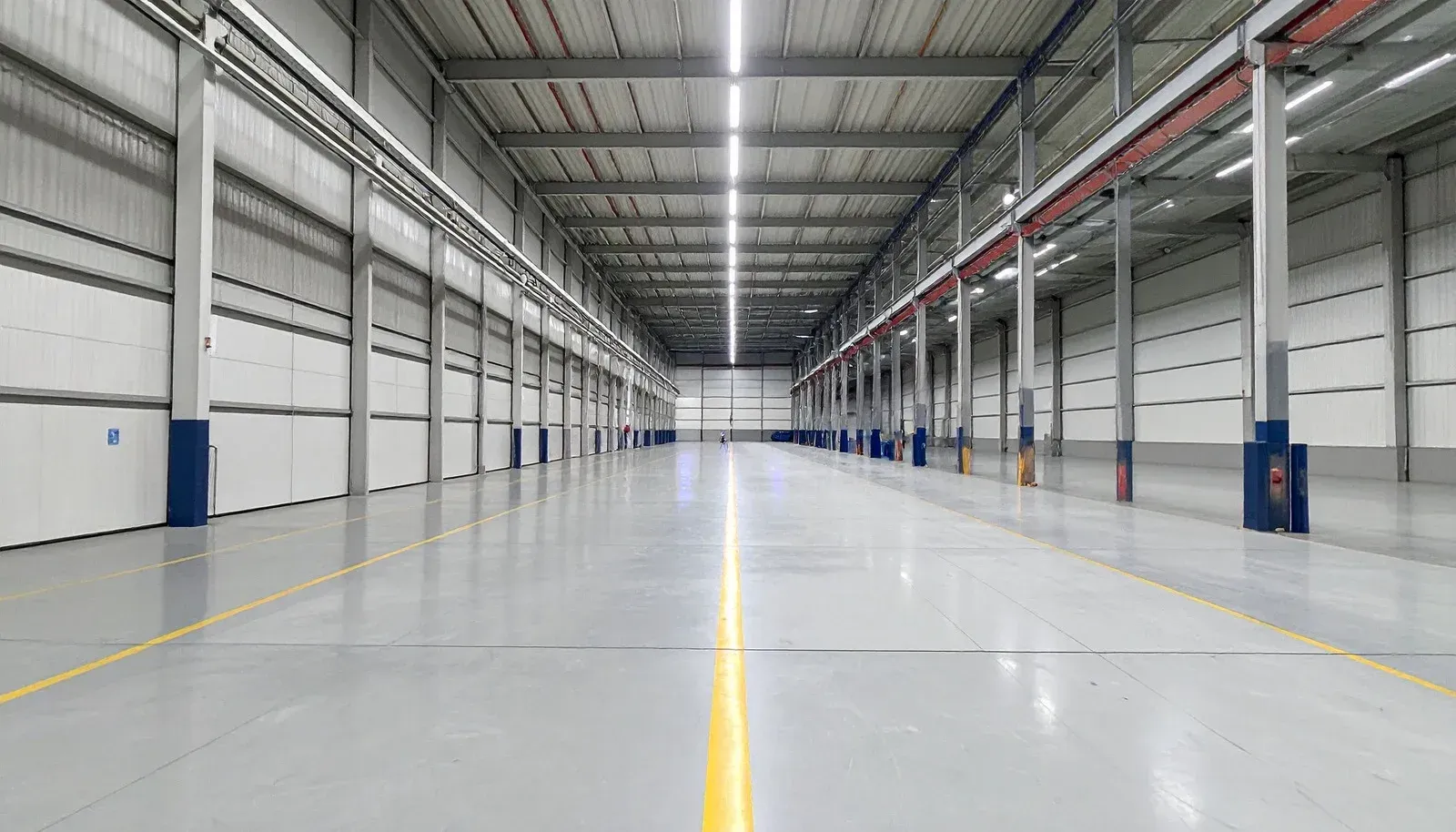 Empty warehouse interior with polished floor, white walls, and rows of steel support columns
