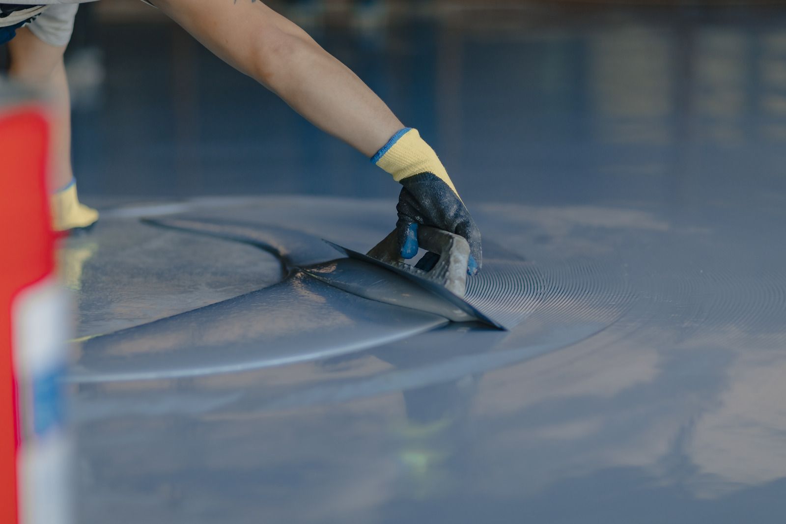 Gloved hand smoothing a blue surface with a squeegee or scraper outdoors