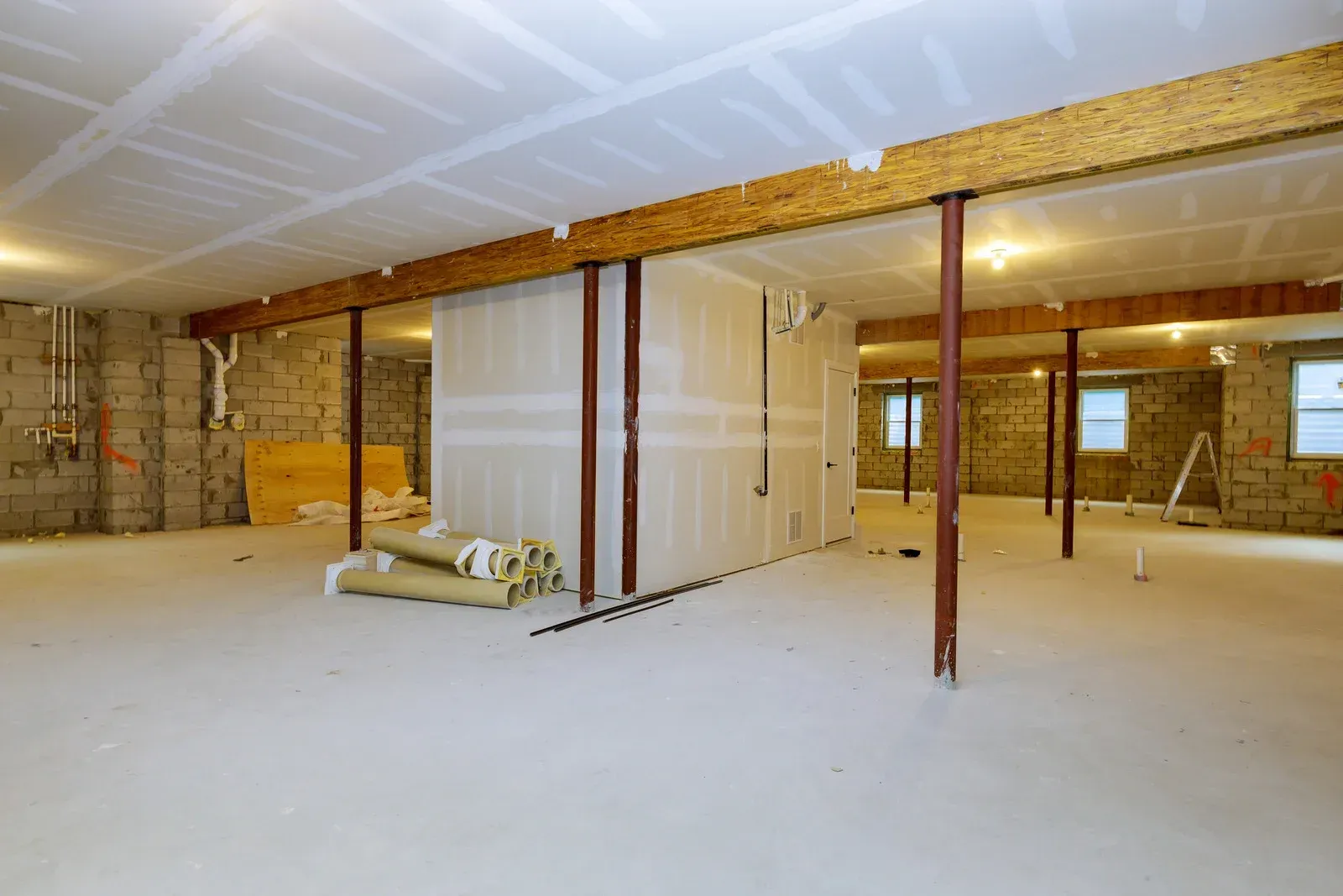 Empty unfinished basement with concrete floor, exposed beams, and a partially framed wall panel