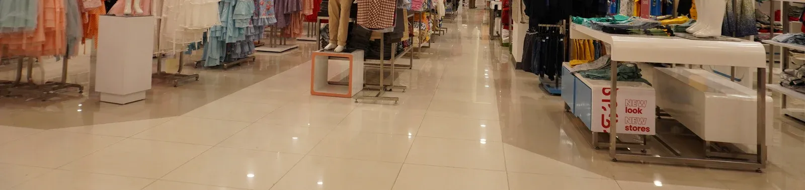 Bright store interior with glossy floors, clothing racks, and display tables in a wide aisle