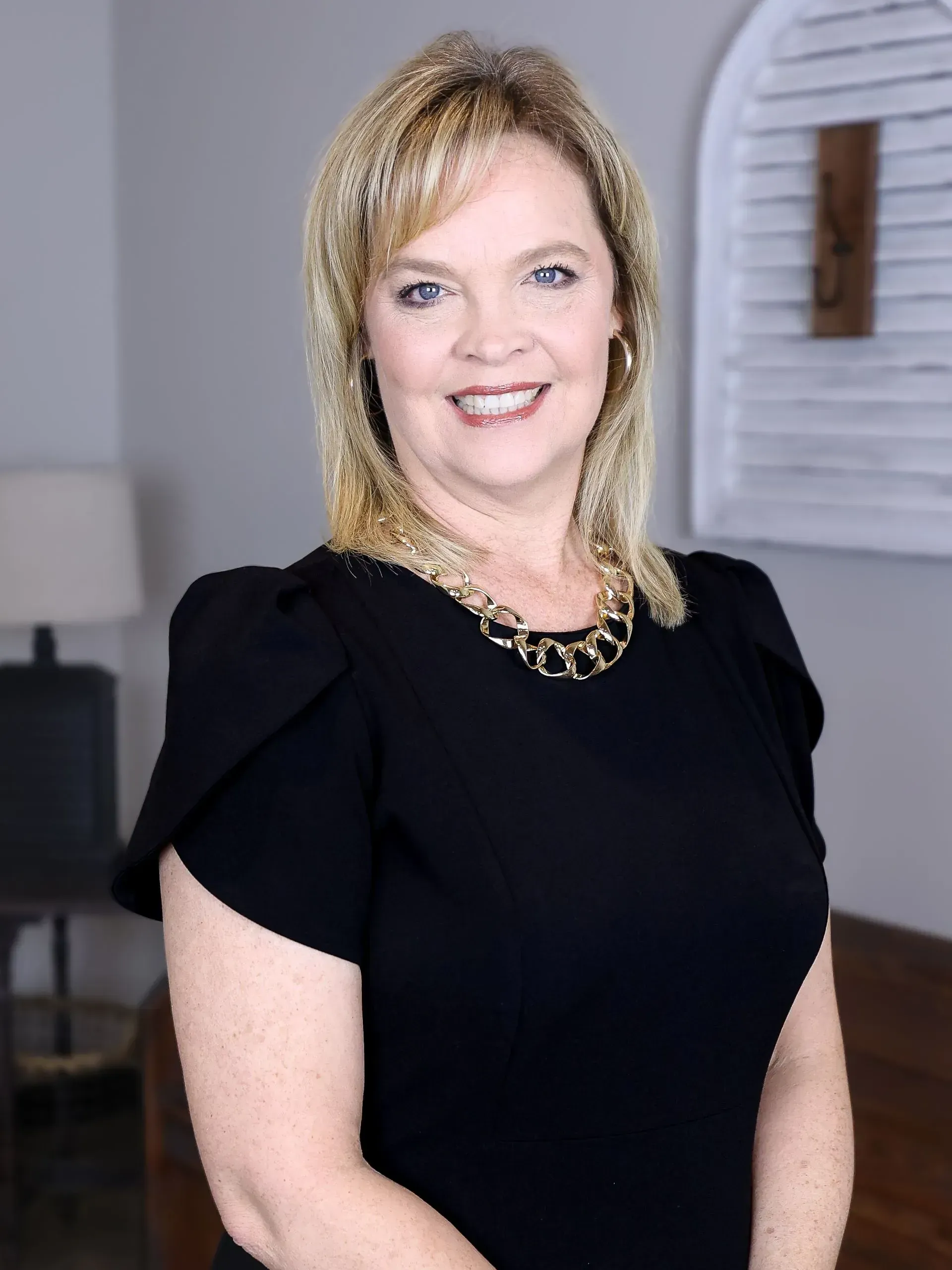 A woman in a black dress and gold necklace is smiling for the camera.