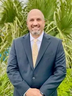 A man in a suit and tie is standing in front of a palm tree.