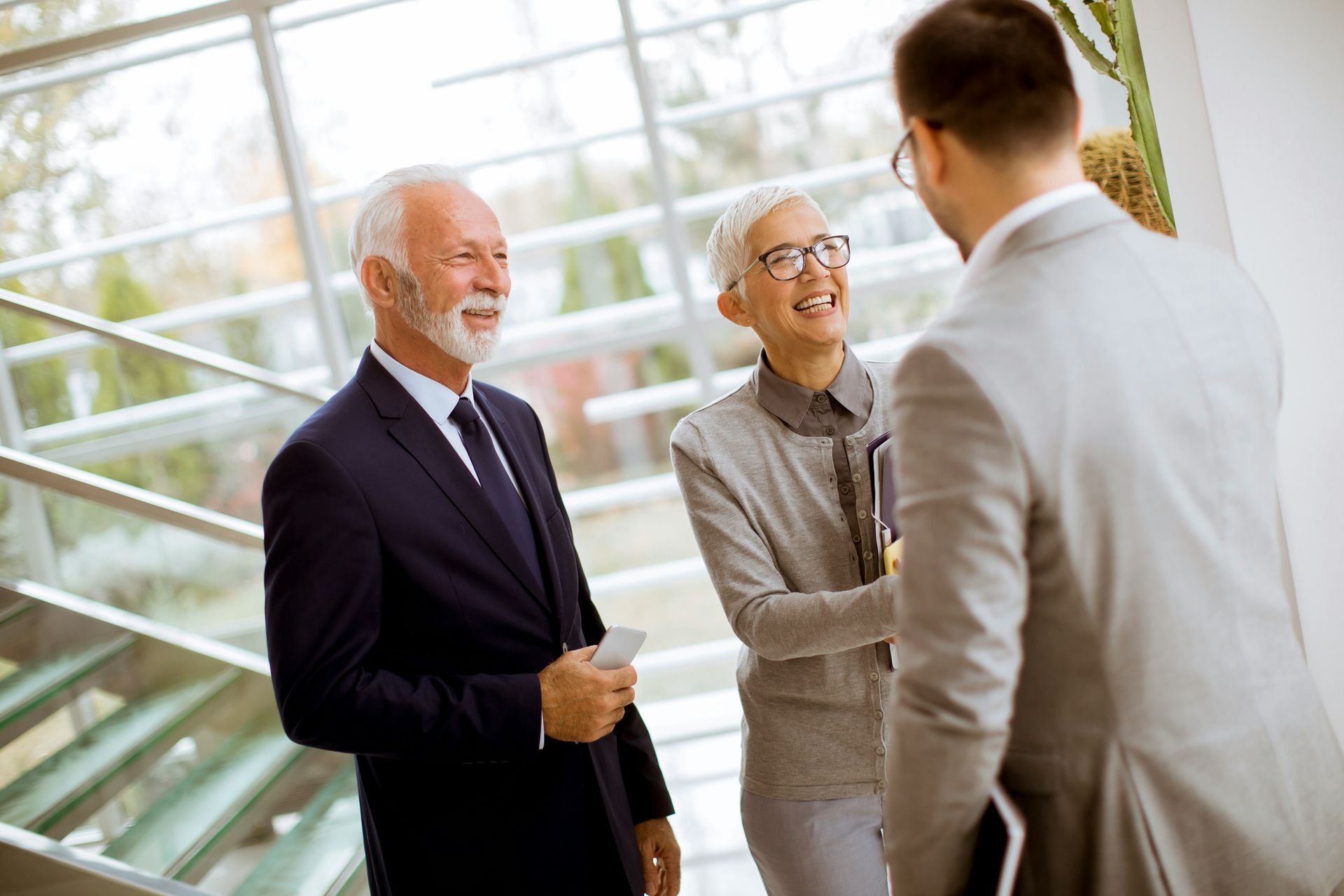 Three professionals smiling and talking in a bright glass office lobby