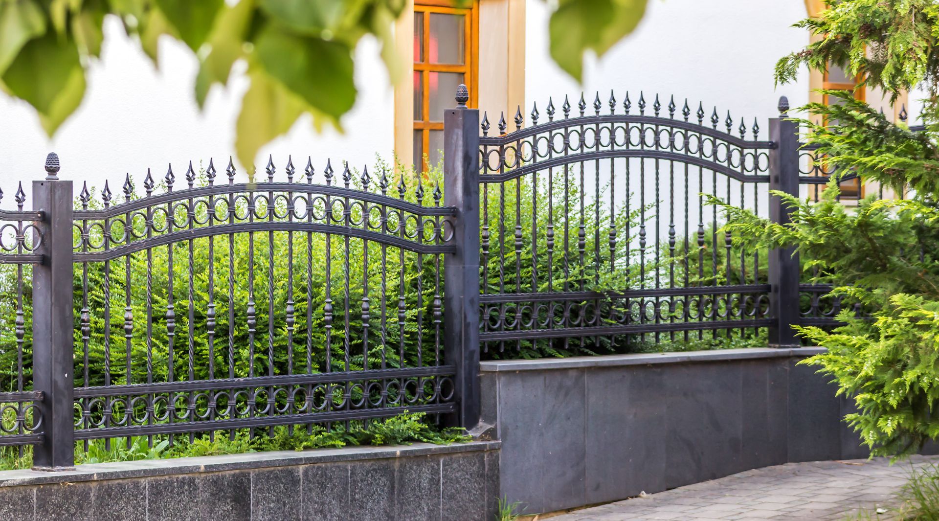 A wrought iron fence is surrounded by trees and bushes in front of a house.