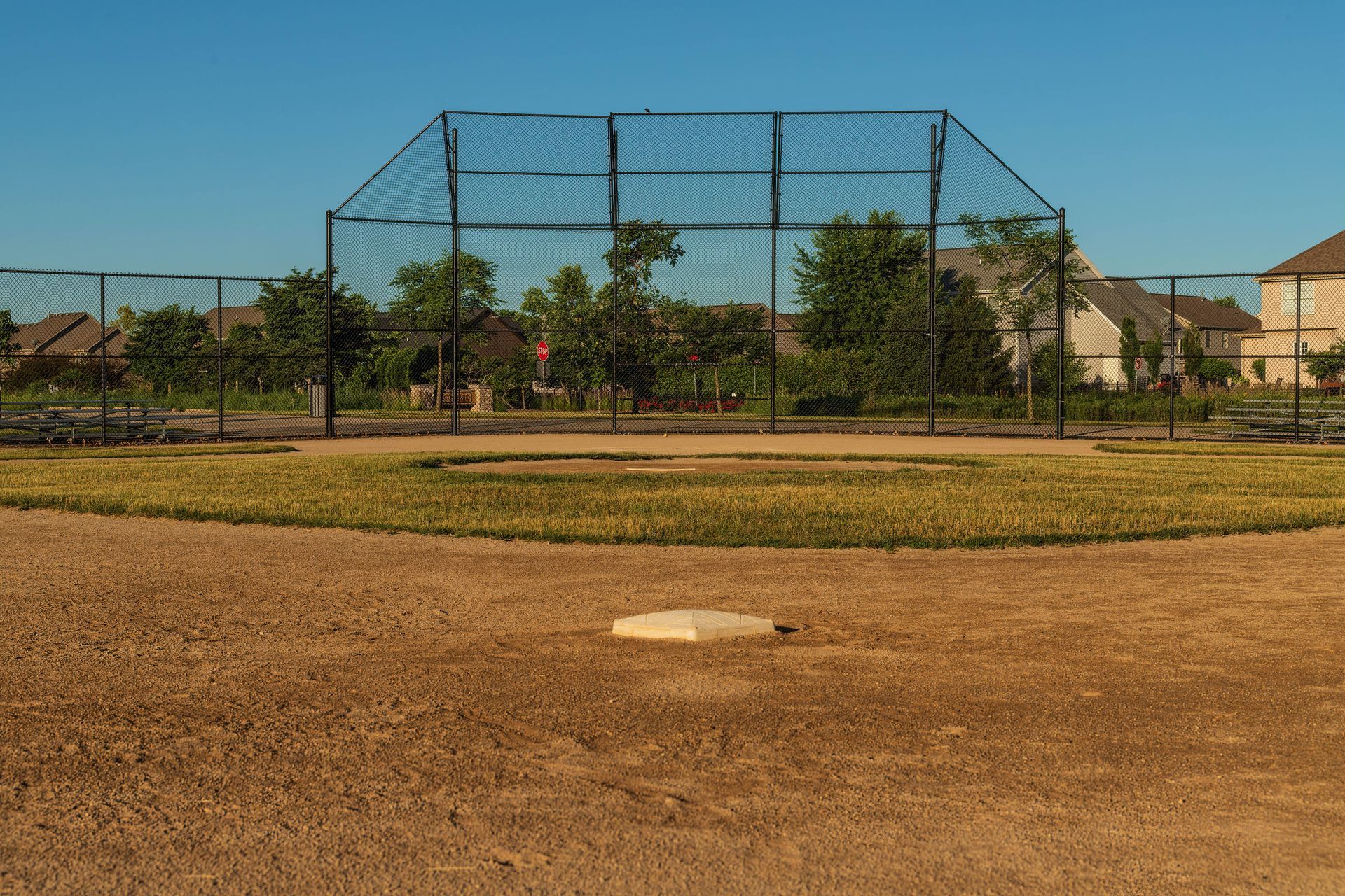 An empty baseball field with a fence and a base An empty baseball field with a fence and a base