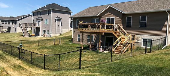 A large house with a deck and stairs is surrounded by a chain link fence. A large house with a deck and stairs is surrounded by a chain link fence.