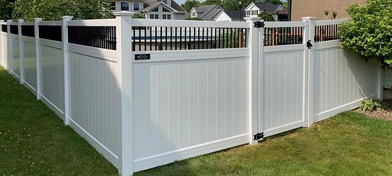 A white vinyl fence with a black gate in a backyard. A white vinyl fence with a black gate in a backyard.