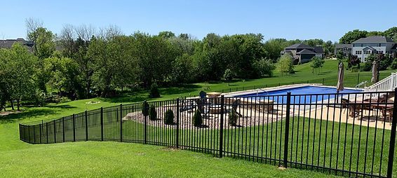 A black fence surrounds a swimming pool in a backyard. A black fence surrounds a swimming pool in a backyard.