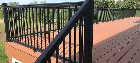 A wooden deck with a black railing and stairs leading up to it. A wooden deck with a black railing and stairs leading up to it.