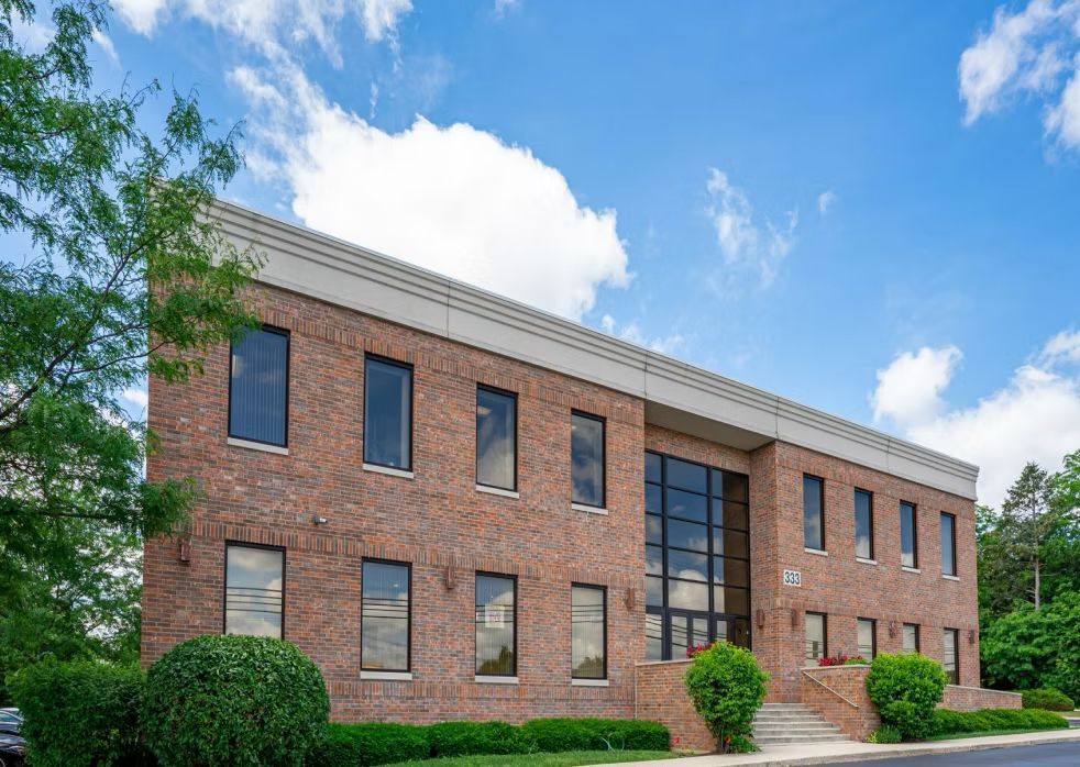 Brick office building with large windows under a blue sky with fluffy clouds.