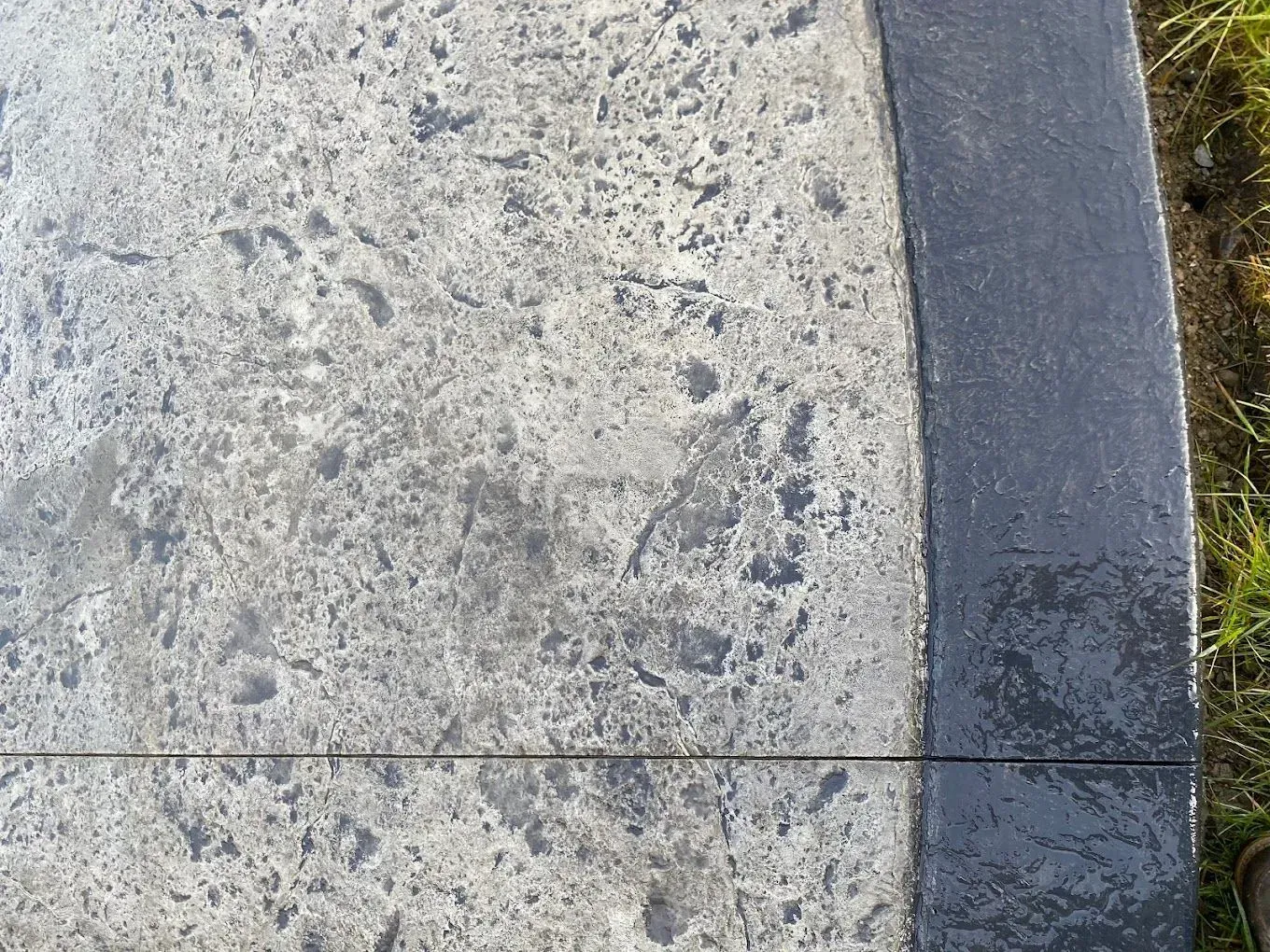 Close-up of a worn concrete sidewalk with a crack and a curved dark edge on the right.