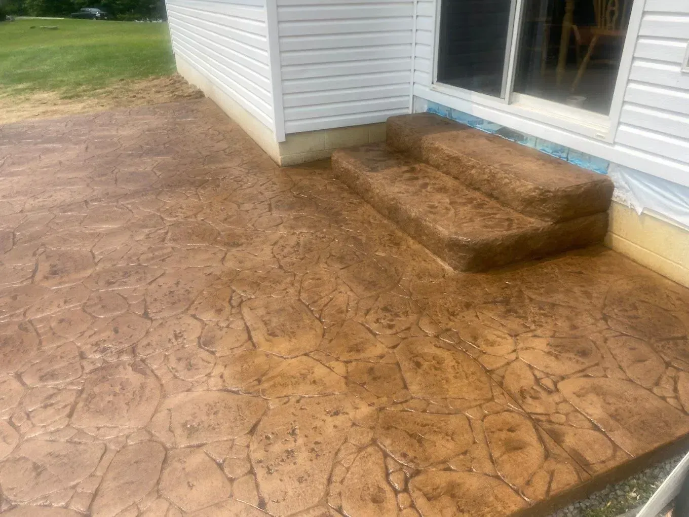 Stamped concrete patio beside white house with two brick steps and sliding glass door