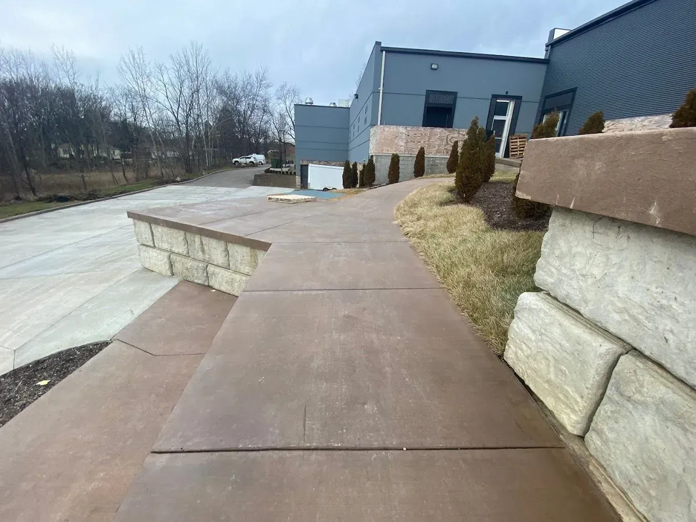 Concrete walkway beside a blue building and retaining wall on a cloudy day