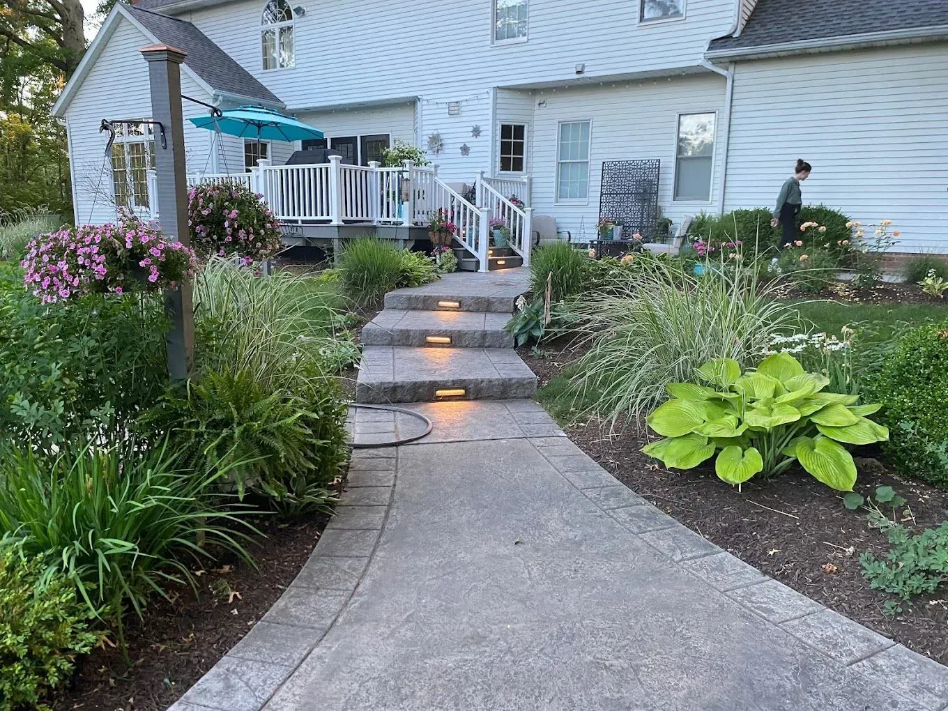 Curved garden walkway with stone steps leading to a house porch, lined with flowering plants and greenery