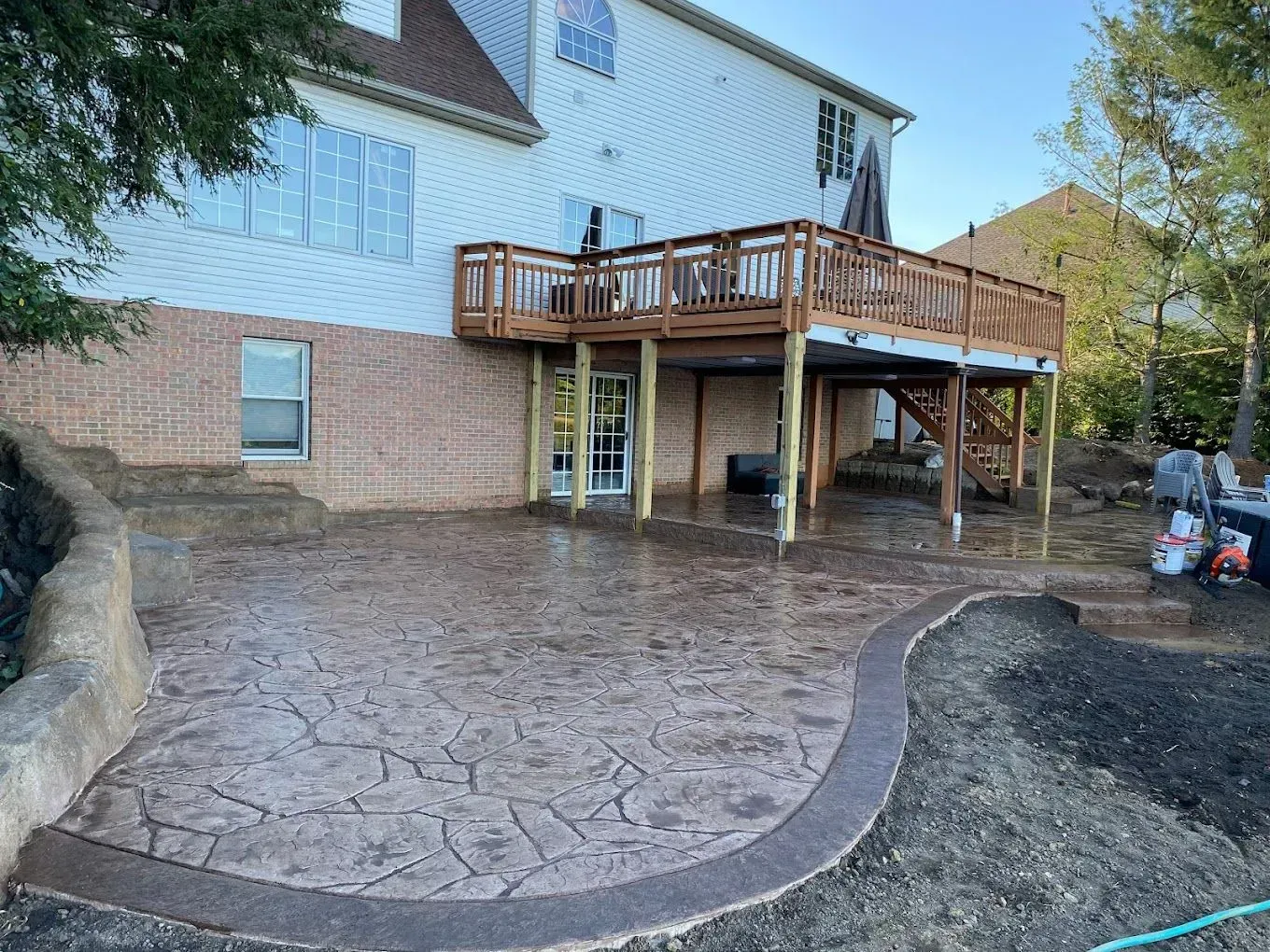 Backyard patio with stamped concrete, a wooden deck, and a brick house exterior