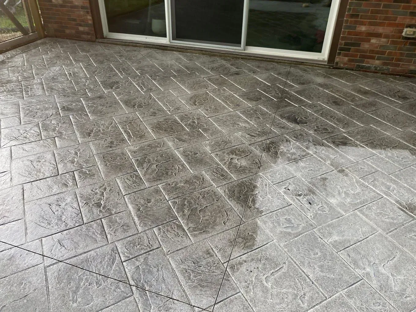 Wet concrete patio with stamped stone pattern outside a glass door