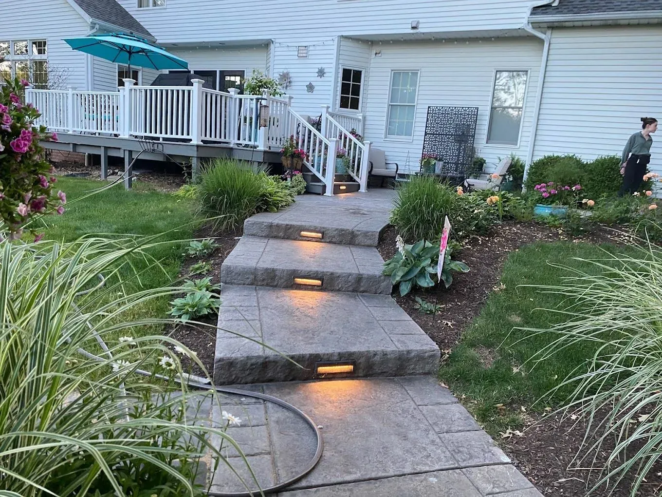 Front garden stone steps leading to a white house, with lit step lights and landscaped plants.