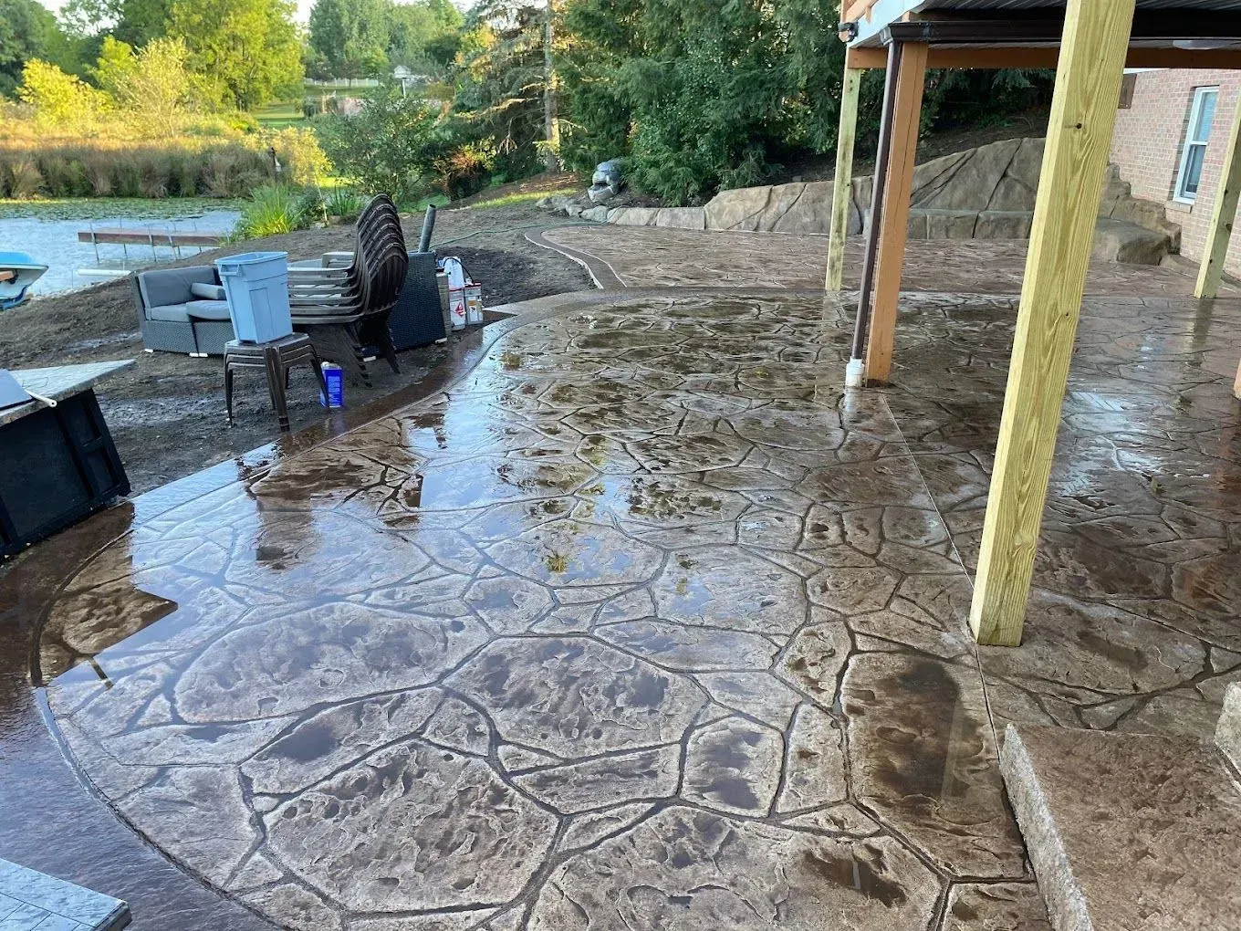 Wet stamped-concrete patio beside a pool, with outdoor furniture and a covered porch after rain.