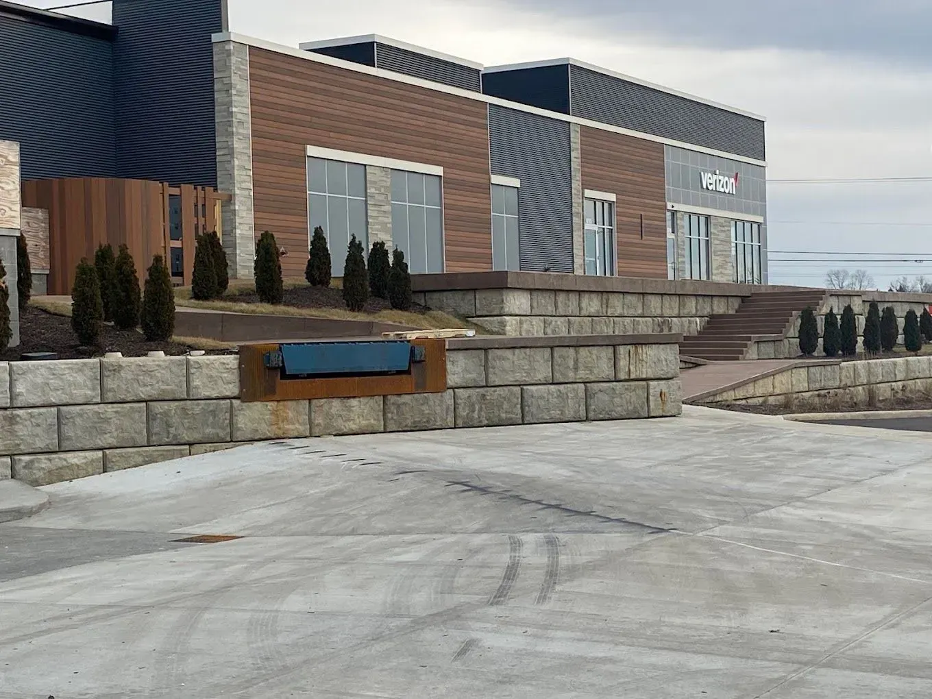 Modern brick building with stone retaining wall, blue sign, and snowy pavement outside
