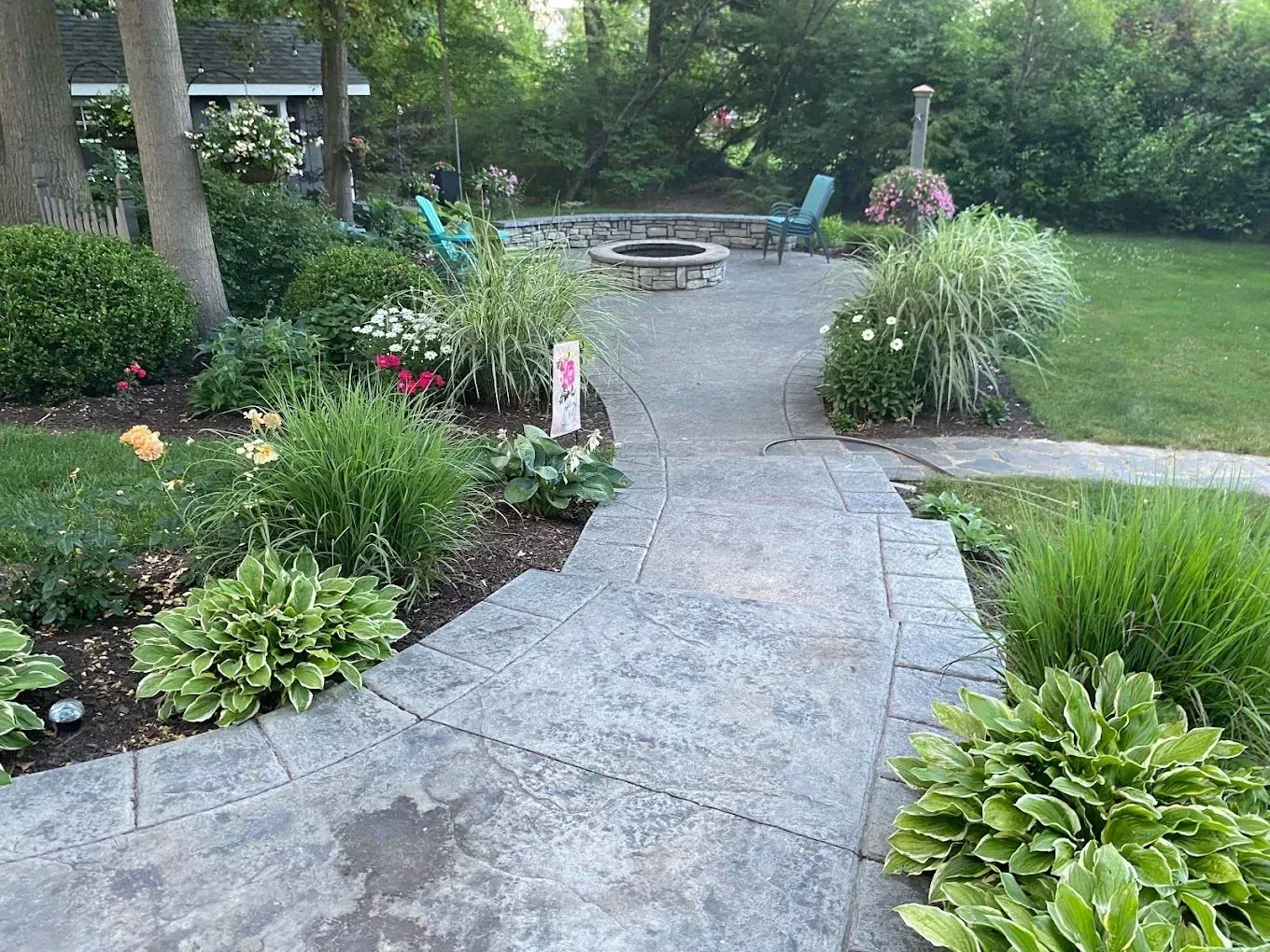 Curved stone garden path leading to a patio with lush green plants and shrubs