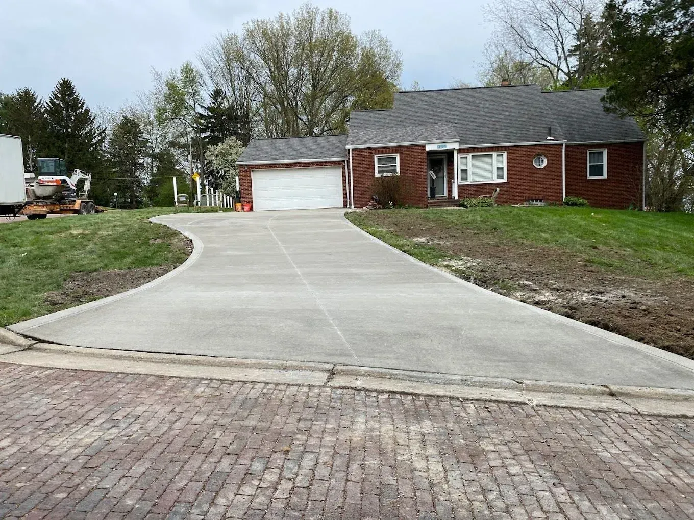 Red brick house with a wide concrete driveway and attached garage, viewed from the street