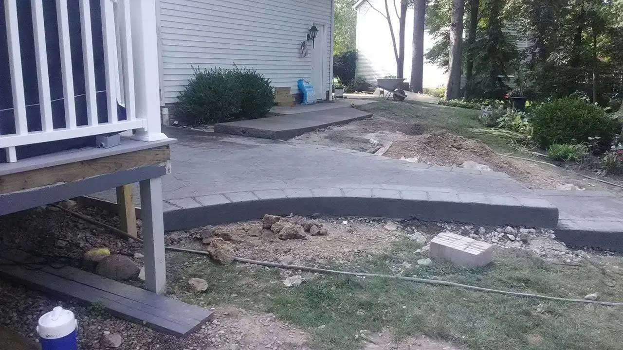Damaged concrete walkway beside a house, with a large broken section and dirt beneath exposed.