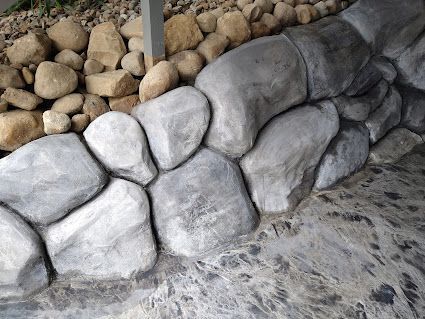 Gray stone wall beside a dirt path, with rounded rocks stacked along the base.