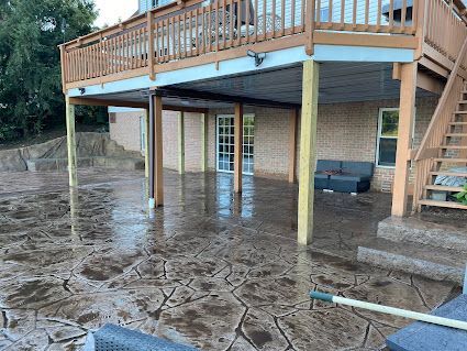 Flooded backyard under a raised wooden deck beside a brick house, with muddy water covering the ground.