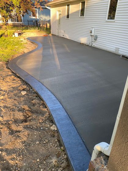Fresh gray concrete walkway curves beside a white house, bordered by a dark blue edge.