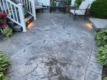Weathered stone patio with cracks, flanked by white railing, potted flowers, and outdoor chairs.