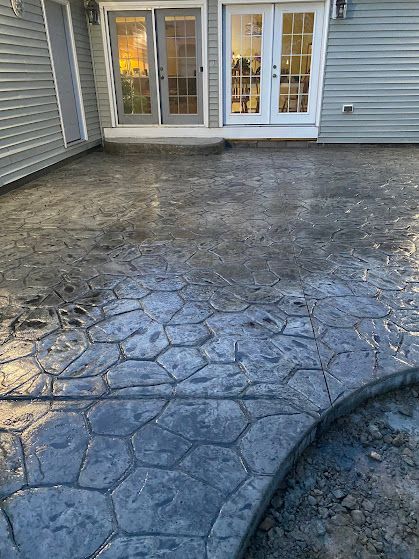 Stamped concrete patio in front of glass doors, with a cracked patch and a hose at the right edge