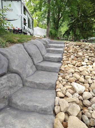 Stone steps beside a rock-lined creek under green trees, with a house in the background