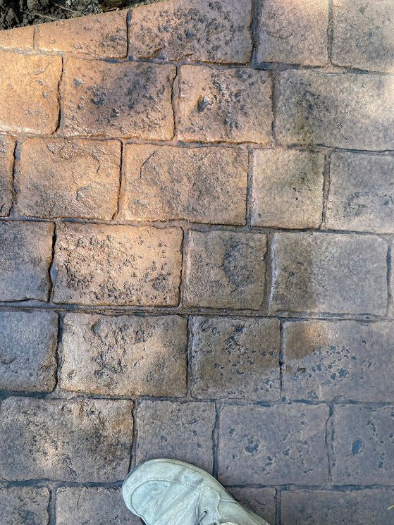 Stone wall lit by sunlight, with the top of a white sneaker visible at the bottom edge.