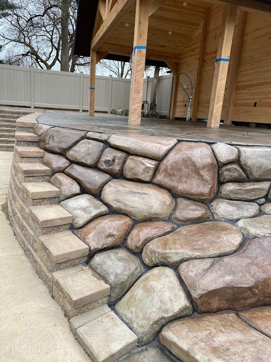 Stone retaining wall and steps beside a wooden deck and concrete patio outdoors