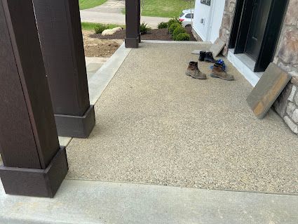 Front porch with tan carpet, dark columns, and two pairs of shoes near the door.