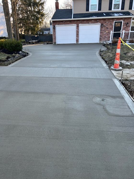 Concrete driveway leading to a two-car garage, with an orange traffic cone on the right side.