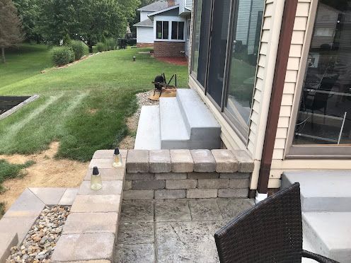 Backyard patio steps and stone walkway beside a house, with a chair in the foreground