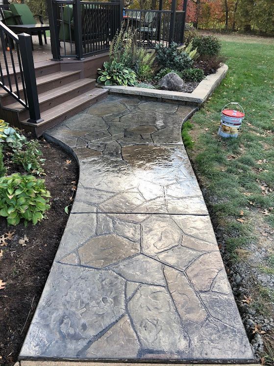 Stone walkway leading to a porch, with a damaged section near a garden bed and lawn.