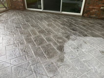 Wet stamped concrete patio beside a brick wall and sliding glass door