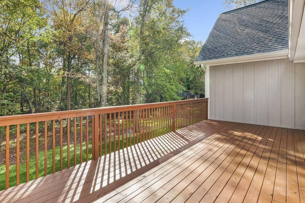 An empty deck with a wooden railing and trees in the background.