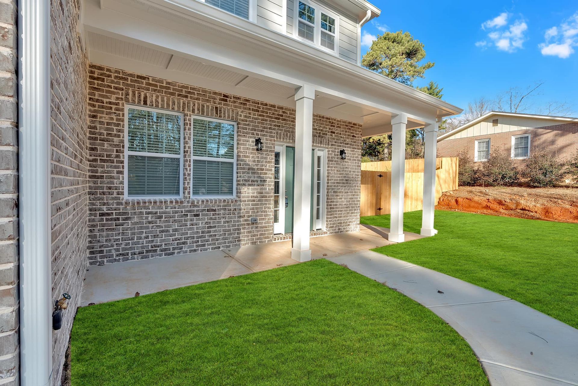 A brick house with a large porch and a lush green lawn.