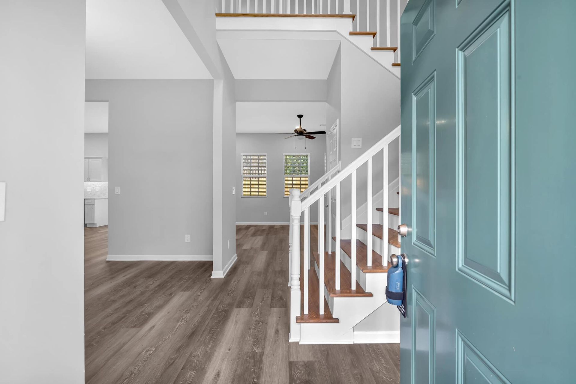 A blue door is open to a hallway with stairs and a ceiling fan.